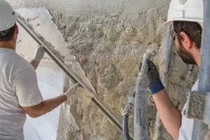 Deux applicateurs projettent l'enduit isolant Fixit 222 Aerogel sur une façade et enlèvent l'enduit isolant haute performance à l'aide d'une latte.