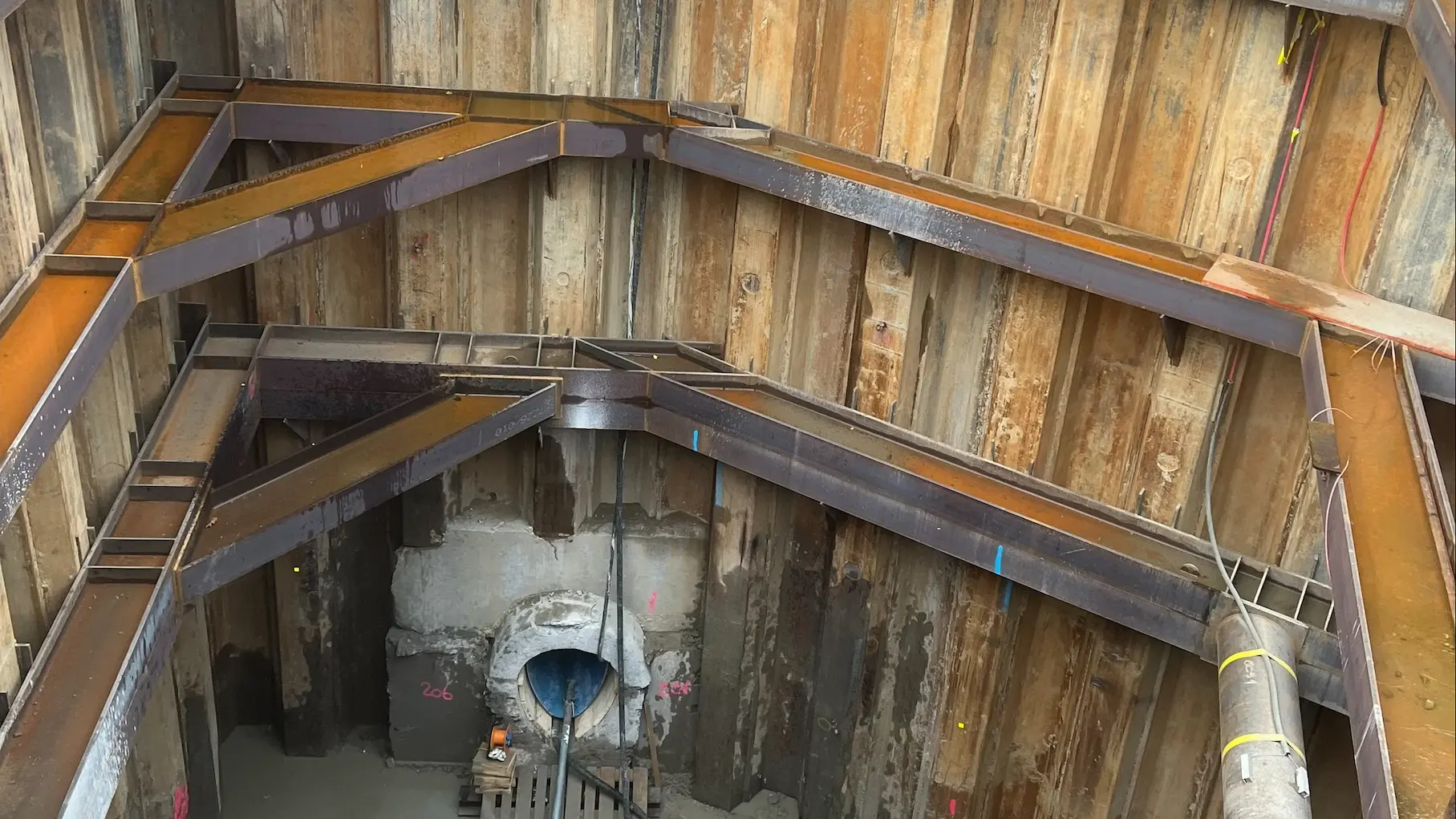 Sicht von oben in die gesicherte Baugrube mit dem Kanalausgang und Inliner am unteren Bildrand