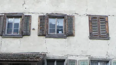 Façade extérieure délabrée avec des fissures horizontales profondes au-dessus des fenêtres et des fissures verticales le long des fenêtres