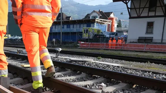 Zone de voie ferrée à la gare de Schwyz avec des ouvriers au premier plan et le silo de béton mousse Fixit POR à l'arrière-plan pour le remplissage d'une conduite souterraine de 50 mètres de long.