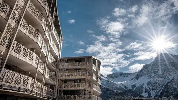 Hotel in den Bergen bei Sonnenschein im Winter mit Bergpanorama und Schnee im Hintergrund