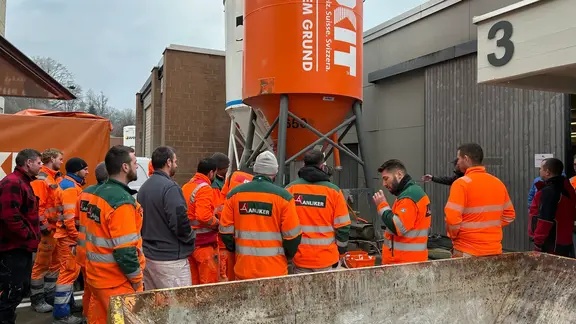 Eine Gruppe in orangener Sicherheitskleidung steht um das Fixit POR Silo versammelt herum