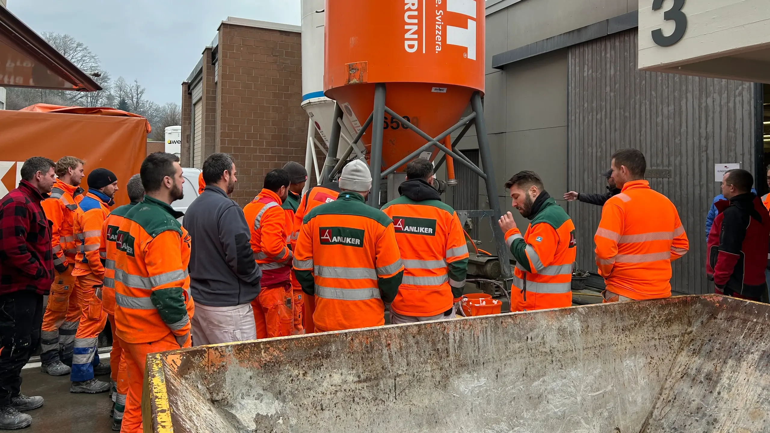 Eine Gruppe in orangener Sicherheitskleidung steht um das Fixit POR Silo versammelt herum