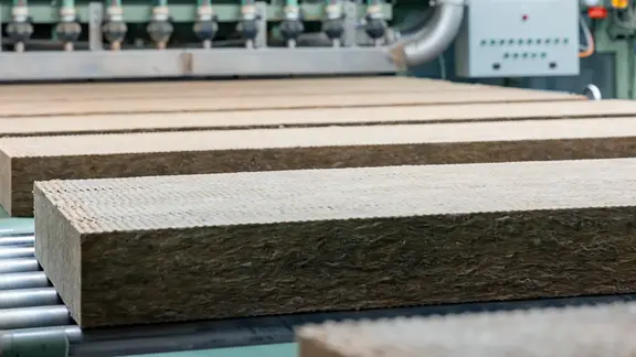 Des panneaux isolants en laine de pierre découpés passent sur un tapis roulant dans la halle de production de Flumroc