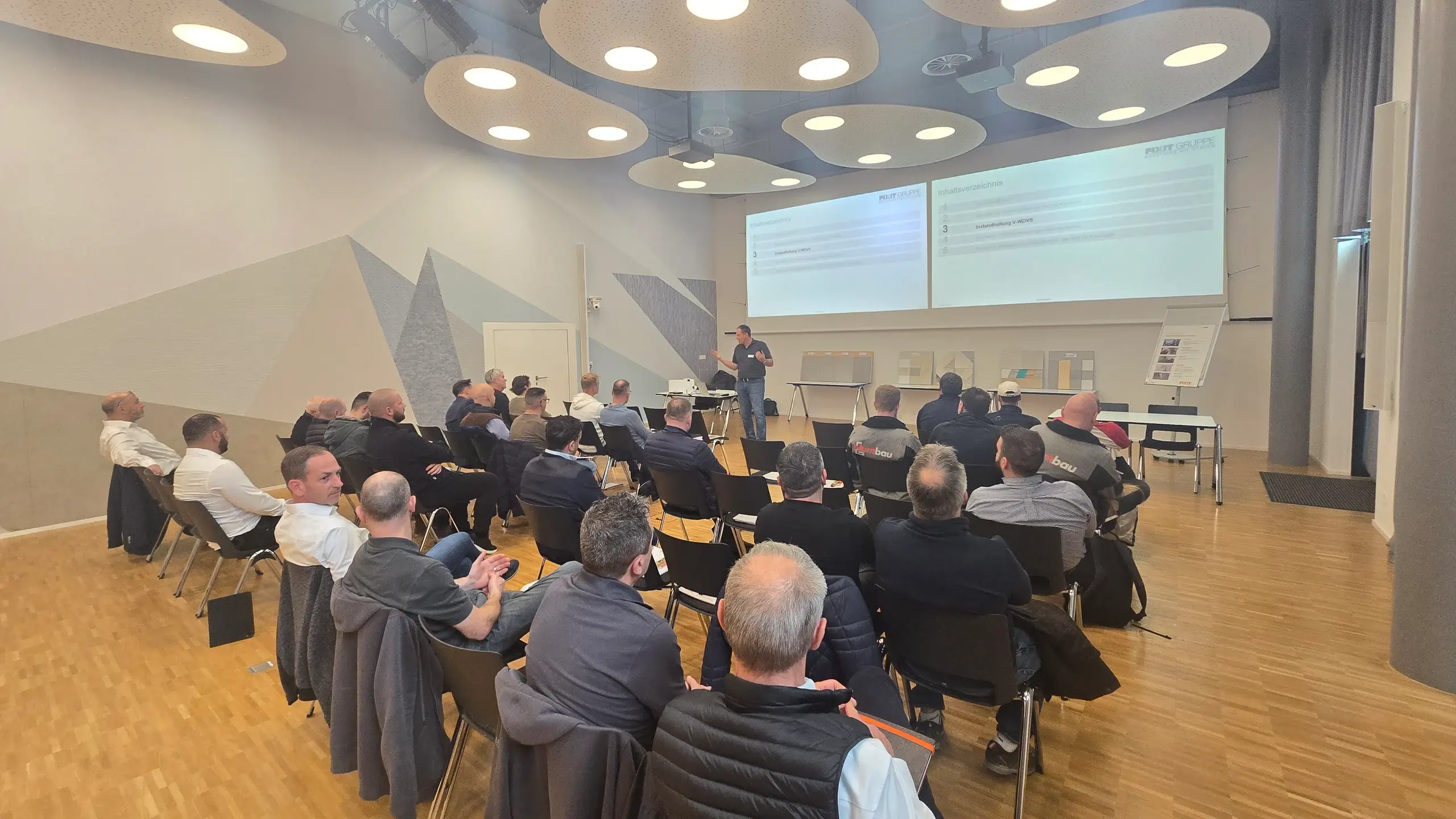 Photo grand angle de la salle de séminaire de l'association suisse des entrepreneurs de construction de façades (SMGV) à Wallisellen avec les invités et les présentations de Fixit