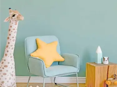 Vor einer hellgrünen Wand befinden sich ein Sessel, ein kleiner Tisch und Spielzeuge