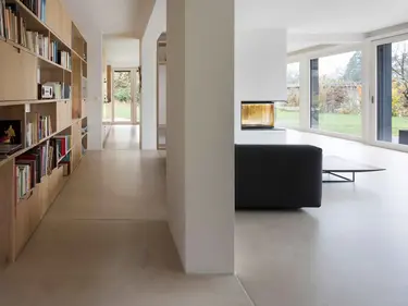 Salon moderne avec grande étagère en bois pour les livres à gauche, murs et plafond en plâtre.
