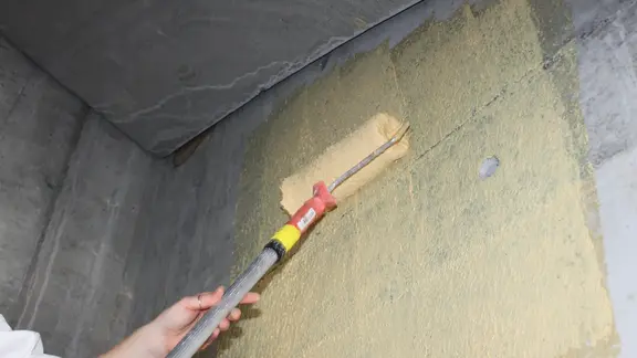 Le pont d'adhérence en quartz Fixit 341 Combi R+S teinté en jaune est appliqué au rouleau sur un mur en béton.
