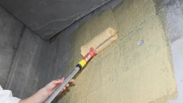 Die gelb eingefärbte Fixit 341 Combi Quarzhaftbrücke R+S wird mit der Rolle auf eine Betonwand appliziert
