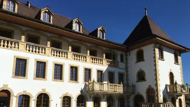 Un grand bâtiment historique crépi de blanc avec des arcs en plein cintre en grès au-dessus des fenêtres et une tour